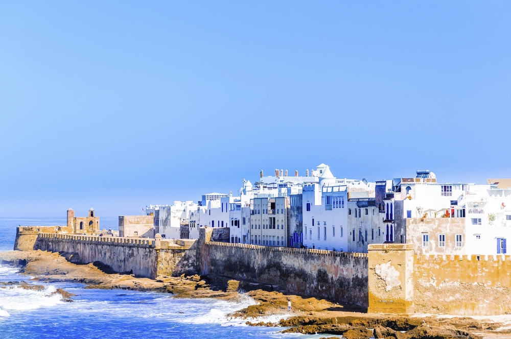Küstenstadt Essaouira in Marokko mit weißen Häusern auf einer Stadtmauer am Atlantik und Felsen im Vordergrund